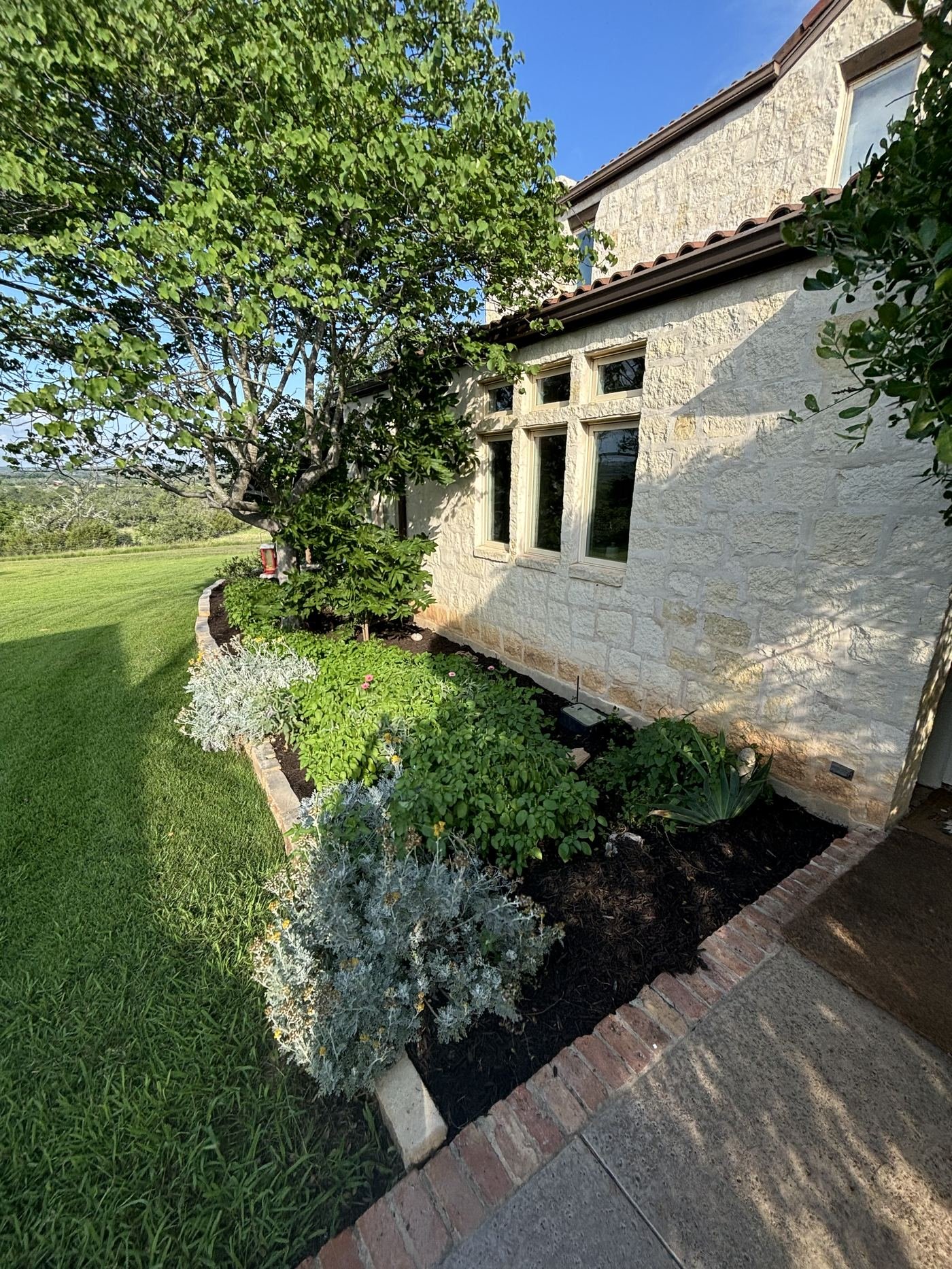 Landscaped grounds of a stone Hill Country home, second angle
